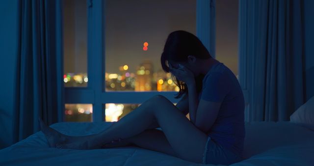 한 여자가 얼굴을 가리고 침대에 앉아 있다