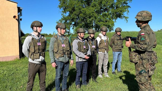 폴란드 국기가 새겨진 군복 차림의 군인으로부터 총을 다루는 법을 배우고 있는 사람들의 모습