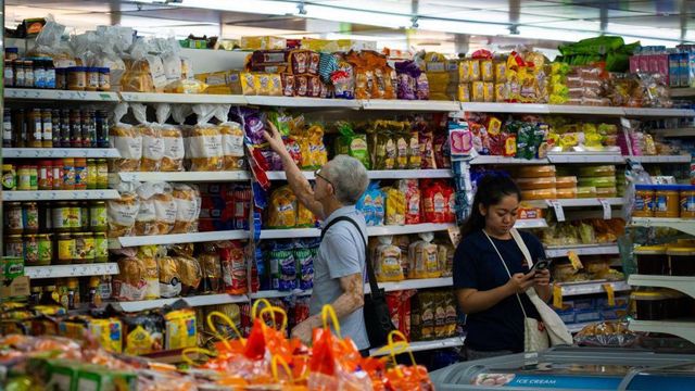 싱가포르의 한 슈퍼마켓에서 한 노인이 포장된 빵 진열대를 둘러보는 동안 옆에서 한 여성이 핸드폰을 확인하고 있다. 