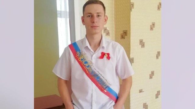 짧은 소매의 흰 셔츠를 입고 어깨에 러시아 국기 색의 어깨끈을 맨 젊은 러시아 남성.