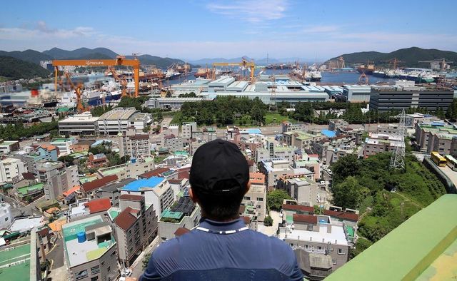 한 시민이 경남 거제시 아주동 주거단지 너머로 한화오션 거제사업장 대형 크레인을 바라보고 있다