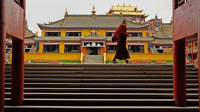 붉은 승복을 입은 승려가 아바의 한 사원 입구를 지나가고 있다