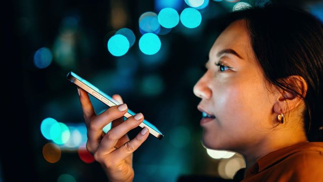 한 젊은 아시아 여성이 밤에 도시의 불빛을 배경으로 휴대폰에 대고 이야기하고 있다