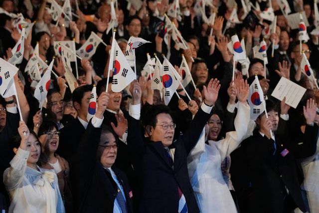한국 이재명 대통령(가운데)이 2025년 8월 15일 서울에서 열린 광복 80주년 기념행사에서 태극기를 흔들며 환호하고 있다.