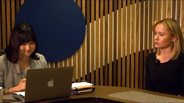 BBC 한국인 기자가 화상 인터뷰를 진행하고 있고, 그 모습을 외국인 여성이 지켜보고 있다