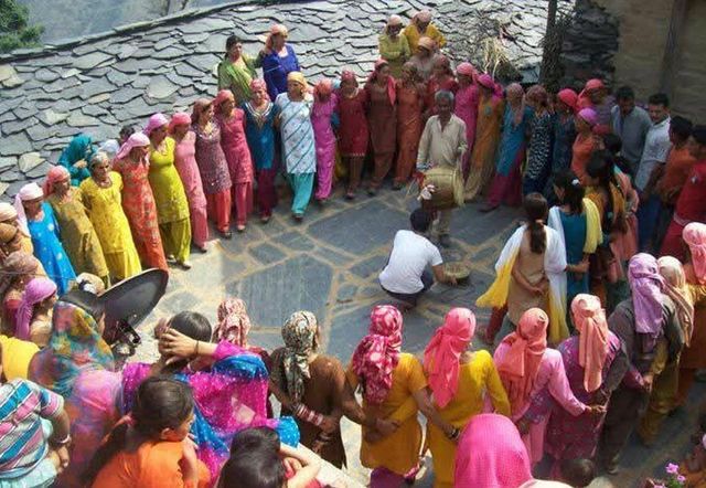 하티 공동체의 수십 명의 여성과 몇 명의 남성이 화려한 옷을 입고 두 명의 남성이 북을 치는 주변에 원을 그리며 서 있다
