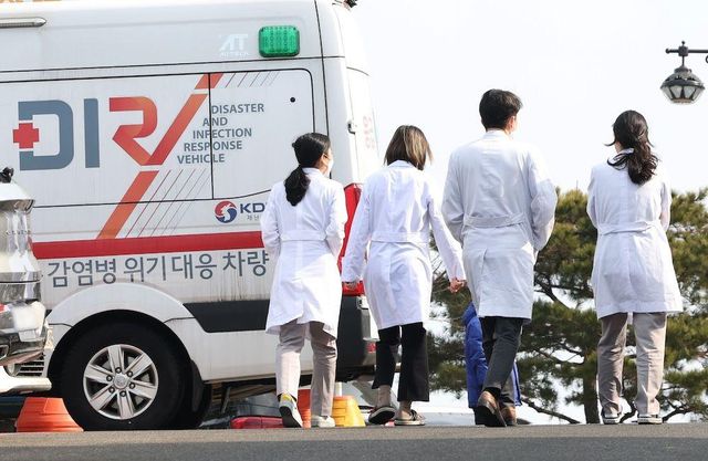 감염병 위기 대응 차량과 의사 가운을 입은 네 명의 의료진의 뒷모습