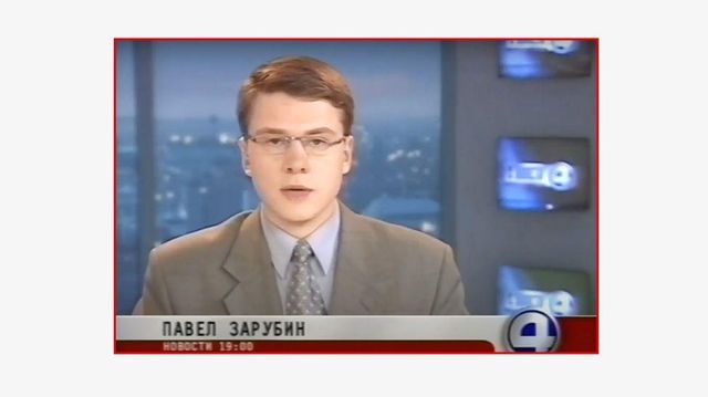 젊은 파벨 자루빈이 러시아 TV 채널에서 화면 오른쪽 하단에 "4" 로고가 있는 뉴스 방송을 진행하고 있다. 자루빈은 회색 넥타이와 안경을 쓴 회색 정장을 입고 있다. TV 화면은 화면 오른쪽 벽 패널에 세로줄로 표시되어 있다. 배경은 도시 스카이라인이다
