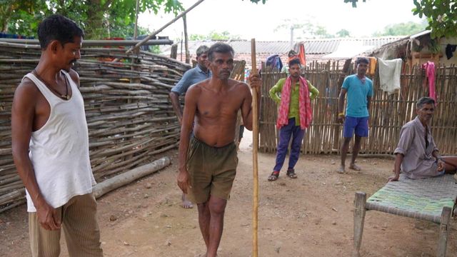 차티스가르 주 바스타르 지역의 한 부지에 서 있는 남성들. 중앙에 있는 남성은 반바지만 입고 막대기를 들고 있으며, 다른 이들은 주변에 서 있다. 