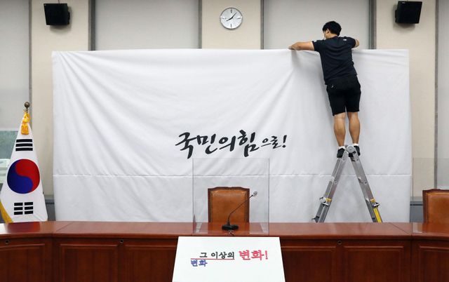 지난 2020년 3월 당명을 '미래통합당'에서 '국민의힘'으로 변경한 국민의힘 담당자가 서울 여의도 국회 당대표회의실의 백드롭 교체 작업을 하고 있다. 배경에는 '국민의 힘으로'라는 글씨가 보인다.