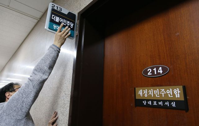 2015년 12월 30일 서울 여의도 국회에서 한 남성이 팔을 높이 들어올려 당명을 바꾼 새정치민주연합 문패를 '더불어민주당'으로 교체하고 있다. 