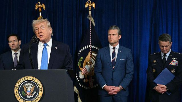 도널드 트럼프 대통령은 파란색 넥타이를 매고 연단에 서서 한 손으로 제스처를 취하며 발언하고 있다. 그의 뒤에는 마르코 루비오 국무장관, 히트 헤그세스 국방장관 그리고 군보고 차람의 댄 케인 미 합참의장이 함께 서 있다