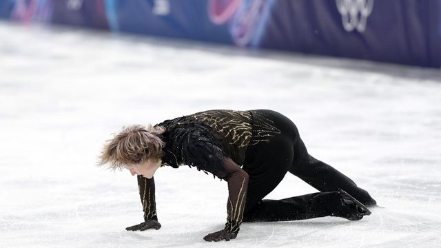 검은색 의상을 입은 피겨 스케이팅 선수 일리아 말리닌이 연기 도중 빙판 위에 넘어져 있다