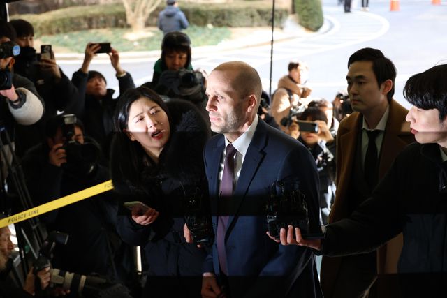 해럴드 로저스 쿠팡 한국 법인 임시대표가 취재진에 둘러싸인 채 질문을 받고 있으며 주변에는 카메라와 녹음 장비를 든 기자들이 모여 있다