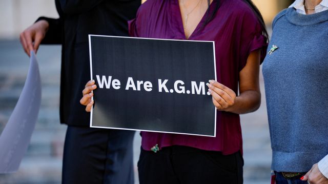보라색 셔츠를 입은 한 여성이 ‘We are K.G.M.’이라고 적힌 팻말을 들고 있다.