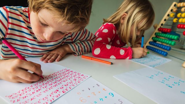 한 소년과 소녀가 책상에 나란히 앉아 색색의 펜으로 종이에 글을 쓰고 있다.