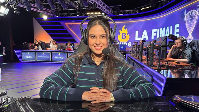한 젊은 여성이 e-스포츠 경기장의 컴퓨터 의자에 앉아 있다. 그는 줄무늬 셔츠를 입고 헤드셋을 착용한 채 카메라를 정면으로 응시하며 미소 짓고 있다. 그의 머리카락은 어두운색이며 길게 늘어져 있다. 그의 뒤로는 프랑스어로 '결승('이라는 단어가 적힌 대형 스크린이 보이며, 그 앞에는 컴퓨터 화면을 마주하고 앉은 체스 선수들이 줄지어 있다