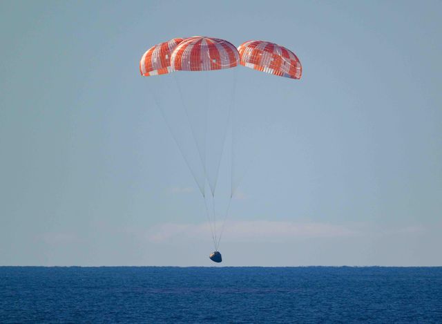 주황색 낙하산을 단 착륙 캡슐이 짙푸른 바다 위로 내려오고 있다 