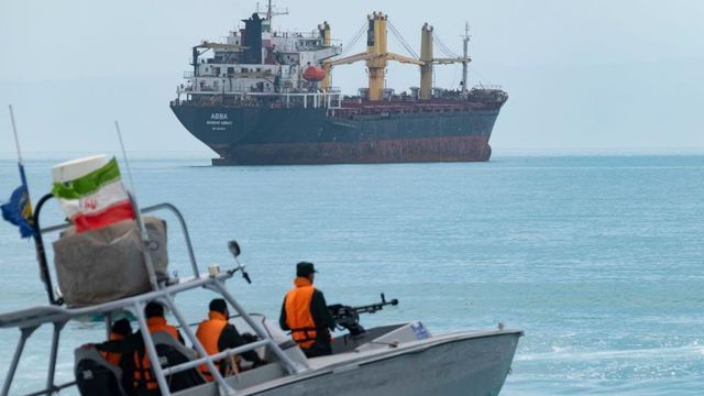 이란 국기가 펄럭이는 작은 순찰선 한 척과 멀리 보이는 대형 선박