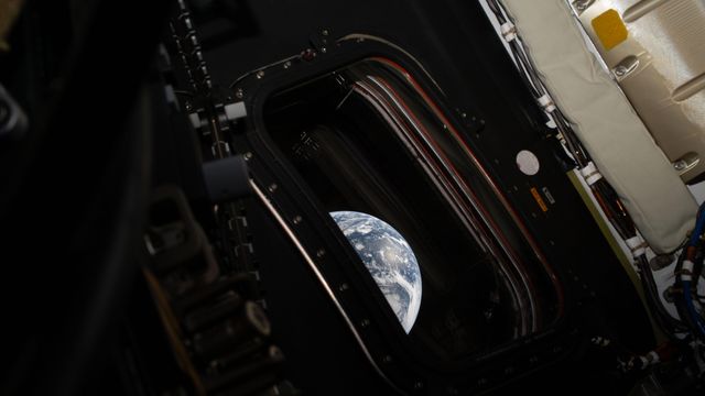 오리온 캡슐 내부에서 촬영된 이미지로, 작은 창문 하나가 보이며 그 밖으로 지구의 일부가 보인다.