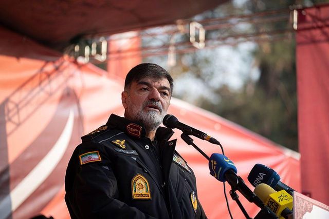 붉은 배경 앞 야외 무대에 선 아흐마드‑레자 라단 준장이 2025년 11월 24일 여러 개의 마이크를 향해 연설하고 있다