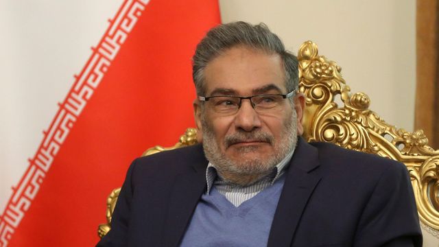 짙은 파란색 재킷에 연한 파란색 브이넥 니트, 연한 파란색과 흰색 줄무늬의 오픈넥 셔츠, 그리고 안경을 착용한 알리 샴카니 해군 소장은 2021년 12월 6일 테헤란에서 타흐눈 빈 자예드 알 나흐얀 아랍에미리트 국가안보보좌관과의 회담 중, 이란 국기 앞에 놓인 금빛 장식 의자에 앉아 있다