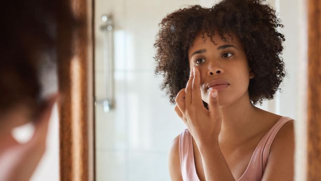 침울한 표정으로 거울을 보며 눈가를 만지는 젊은 여성