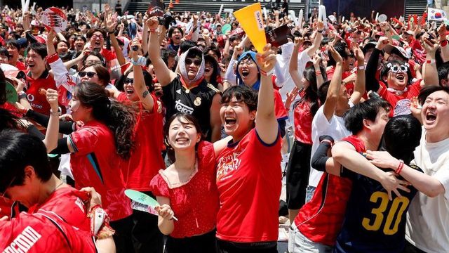 붉은 옷을 입고 축구를 응원하는 사람들이 기뻐하고 있다
