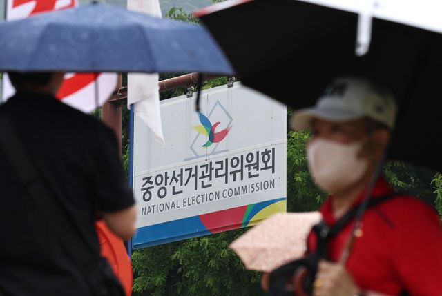 우산을 쓴 시민들이 '중앙선거관리위원회'라고 적힌 표지판 앞을 지나고 있다