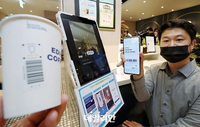 지난해 5월 서울 중구 이디야커피 IBK본점에서 열린 일회용 컵 보증금 제도 시행 공개 시연회에서 환경부 직원이 소비자가 컵을 반납하고 자원순환보증금(300원)을 반환받는 과정을 홍보하고 있다. ⓒ연합뉴스