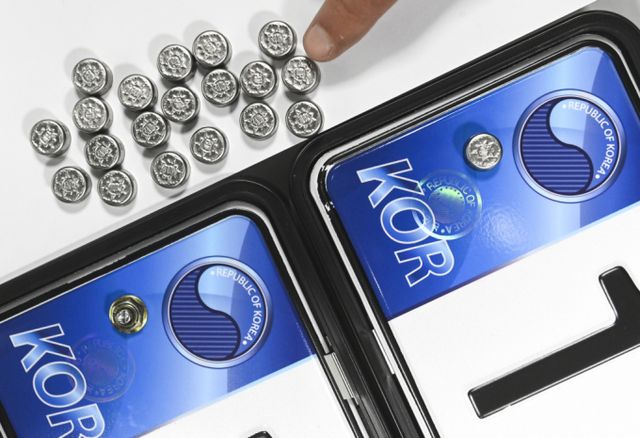 자동차 번호판 봉인제가 오늘부터 폐지된다. 제도 시행 63년만이다. 사진은 자동차 등록번호판 봉인제도 폐지를 하루 앞둔 20일 수원도시공사 번호판제작소에서 관계자가 기존 스테인리스 마개로 봉인된 번호판(사진 오른쪽)과 마개를 제거한 뒤 너트로 고정한 번호판을 보여주고 있는 모습. /사진=뉴시스