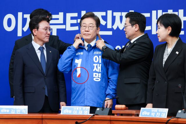 이재명 더불어민주당 대선 후보가 빨간색 점이 찍힌 선거 점퍼를 입어 눈길을 끄는데 보수를 상징하는 빨간색을 사용함으로써 통합 의지를 담아냈다는 분석이다. 사진은 지난 28일 박찬대 더불어민주당 대표 직무대행 겸 원내대표(오른쪽에서 두번째)가 서울 여의도 국회에서 열린 최고위원회의에서 이재명 대선 후보(파란색 점퍼)에게 선거복을 입혀준 뒤 옷깃을 정리하고 있는 모습. /사진=뉴스1
