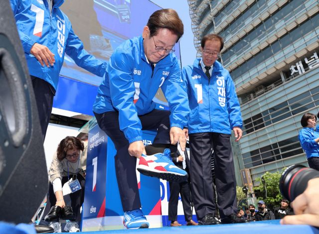 이재명 더불어민주당 대통령 후보가 6·3 대선 공식 선거운동 첫날, 양복과 구두를 벗고 파란색과 빨간색이 섞인 선거운동복과 운동화를 착용하고 유세에 나섰다. 사진은 이재명 더불어민주당 대선후보가 제21대 대통령선거 공식 선거운동이 시작된 12일 오전 서울 청계광장에서 열린 중앙선거대책위원회 출정식에서 운동화를 신고 있는 모습. /사진=공동취재
