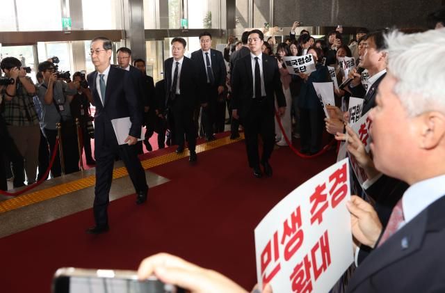 한덕수 대통령 권한대행 국무총리가 24일 추가경정예산안 시정연설을 위해 서울 여의도 국회에 도착해 본회의장으로 향하는 사이 더불어민주당 의원들이 팻말 시위를 하고 있다 사진연합뉴스