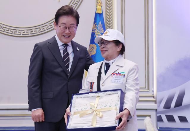 이재명 대통령이 27일 청와대 영빈관에서 열린 호국 보훈의 달 대통령의 초대 행사에서 특별 초청대상자인 이춘자 씨에게 광목이불을 선물한 뒤 기념촬영을 하고 있다 사진연합뉴스