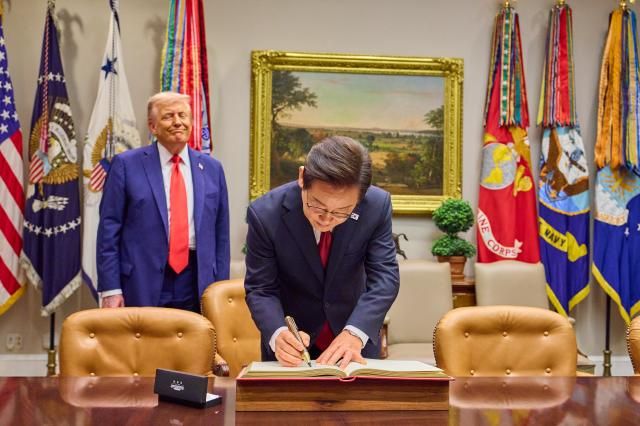  이재명 대통령이 25일현지시간 미국 워싱턴 DC 백악관에서 도널드 트럼프 미국 대통령이 지켜보는 가운데 방명록을 작성하고 있다 사진연합뉴스