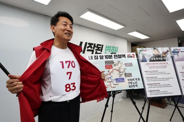 오세훈 국민의힘 서울시장 후보가 26일 서울 종로구 대왕빌딩 선거캠프에서 도시철도 공약을 발표하며 가슴에 붙인 전철역 노선 계획 숫자 티셔츠를 보여주고 있다 사진연합뉴스