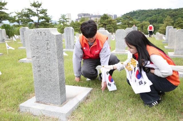 구성원들이 국립서울현충원 묘비 앞에 태극기를 꽂으며 묘역 정화 활동을 실시하고 있다 사진SKC