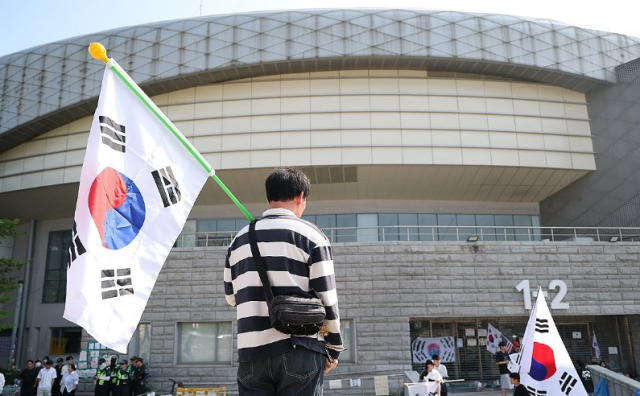 6·3 지방선거 투표용지 부족 사태로 빚어진 잠실 개표소 봉쇄 시위가 이어진 지난 11일 서울 송파구 올림픽공원 핸드볼경기장에서 한 참가자가 태극기를 들고 있다 사진연합뉴스