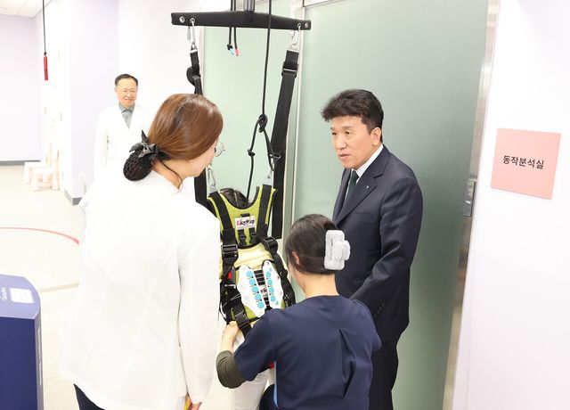 [전달식에 참석한 함영주 회장(사진 맨 오른쪽)이 워킹레일 보행치료를 받고 있는 장애 아동에게 따뜻한 격려의 말을 전하고 있다.]