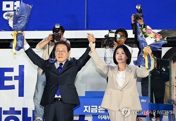 제21대 대통령 당선이 확실시되는 더불어민주당 이재명 대선 후보와 부인 김혜경 여사가 4일 서울 여의도 국회 인근에서 당 주최로 열린 국민개표방송 행사에 참석해 꽃다발을 받고서 시민들을 향해 두 팔을 들어 인사하고 있다. [사진=연합뉴스]