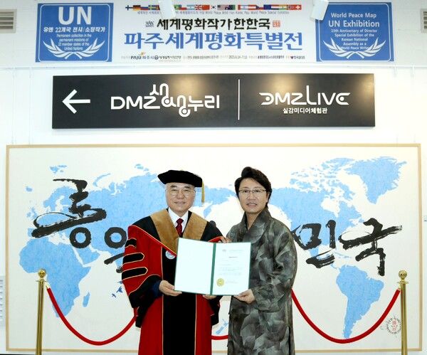 (사진설명 = 한한국 세계평화작가가 전시관에서 박상원 총장으로부터 교수 임명장을 받고 기념 촬영을 하고 있다./ 제공=세계평화사랑연맹)
