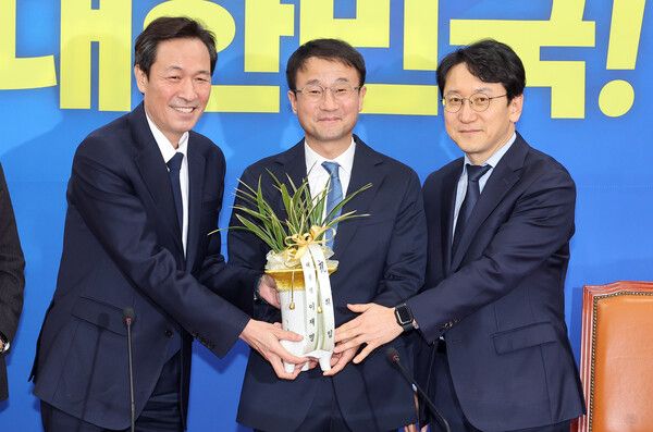더불어민주당 한병도 신임 원내대표(가운데)가 12일 국회에서 우상호 청와대 정무수석을 만나 이재명 대통령의 축하 난을 받고 있다. 오른쪽은 천준호 신임 원내운영수석부대표. [사진=연합뉴스]&nbsp;