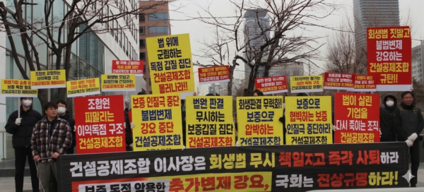 A사 노동조합 조합원들이 국회 앞에서 건설공제조합의 불법 변제 강요 중단을 촉구하는 시위를 벌이고 있다. '법이 살린 기업을 다시 죽이는 조직 건설공제조합'등의 문구가 적혀 있다. 하단 현수막에는 