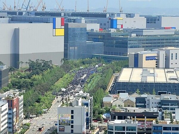 23일 경기도 평택시&nbsp;삼성전자 평택캠퍼스 앞에서 열린&nbsp;삼성전자 노동조합 투쟁 결의대회. 고덕동 삼성전자 사거리의 끝지점으로, 안쪽 사무동과 파운드로 공장 사이로 검정 조끼를 입은 노조원들이 1Km 이상 길게 늘어져 있다. [사진=폴리뉴스 김성지 기자]