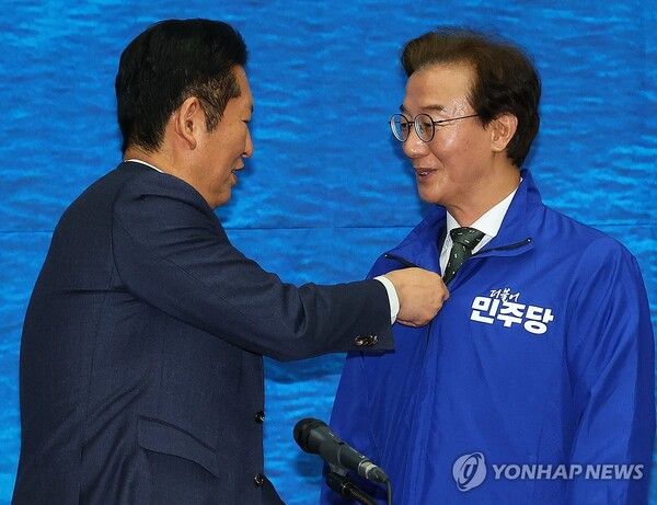 더불어민주당 정청래 대표가 15일 오전 부산 동구 부산항국제전시컨벤션센터에서 열린 부산 현장 최고위원회에서 전재수 부산시장 후보에게 파란 점퍼를 입혀주고 있다.[사진=연합뉴스]