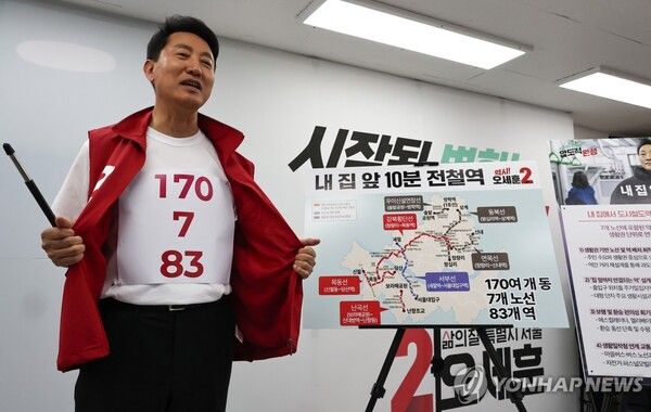 국민의힘 오세훈 서울시장 후보가 26일 서울 종로구 대왕빌딩 선거캠프에서 도시철도 공약을 발표하며 가슴에 붙인 전철역 노선 계획 숫자가 적힌 티셔츠를 보여주고 있다.[사진=연합뉴스]