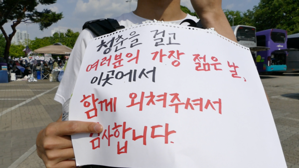 서울 올림픽공원 핸드볼경기장 앞 시위 현장에서 한 대학생이 '청춘을 걸고 여러분의 가장 젊은 날 이곳에서 함께 외쳐주셔서 감사합니다'라는 문구를 적은 종이를 들고 있다. 2026.6.11. [사진=폴리뉴스]