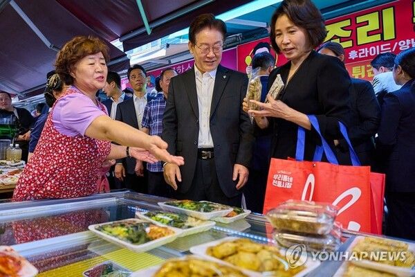 이재명 대통령과 김혜경 여사가 6일 서울 강동구 중앙보훈병원 위문 방문 후 인근 길동복조리시장에서 음식을 사고 있다 [사진=연합뉴스]