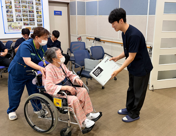 경기 수원시 수원보훈요양원에서 열린 국가유공자 대상 치과 의료봉사 현장에서 경희대학교 치과대학 봉사동아리 '코다(KODA)' 학생이 국가유공자에게 동아제약 검가드 선물세트를 전달하고 있다. [사진=동아제약]